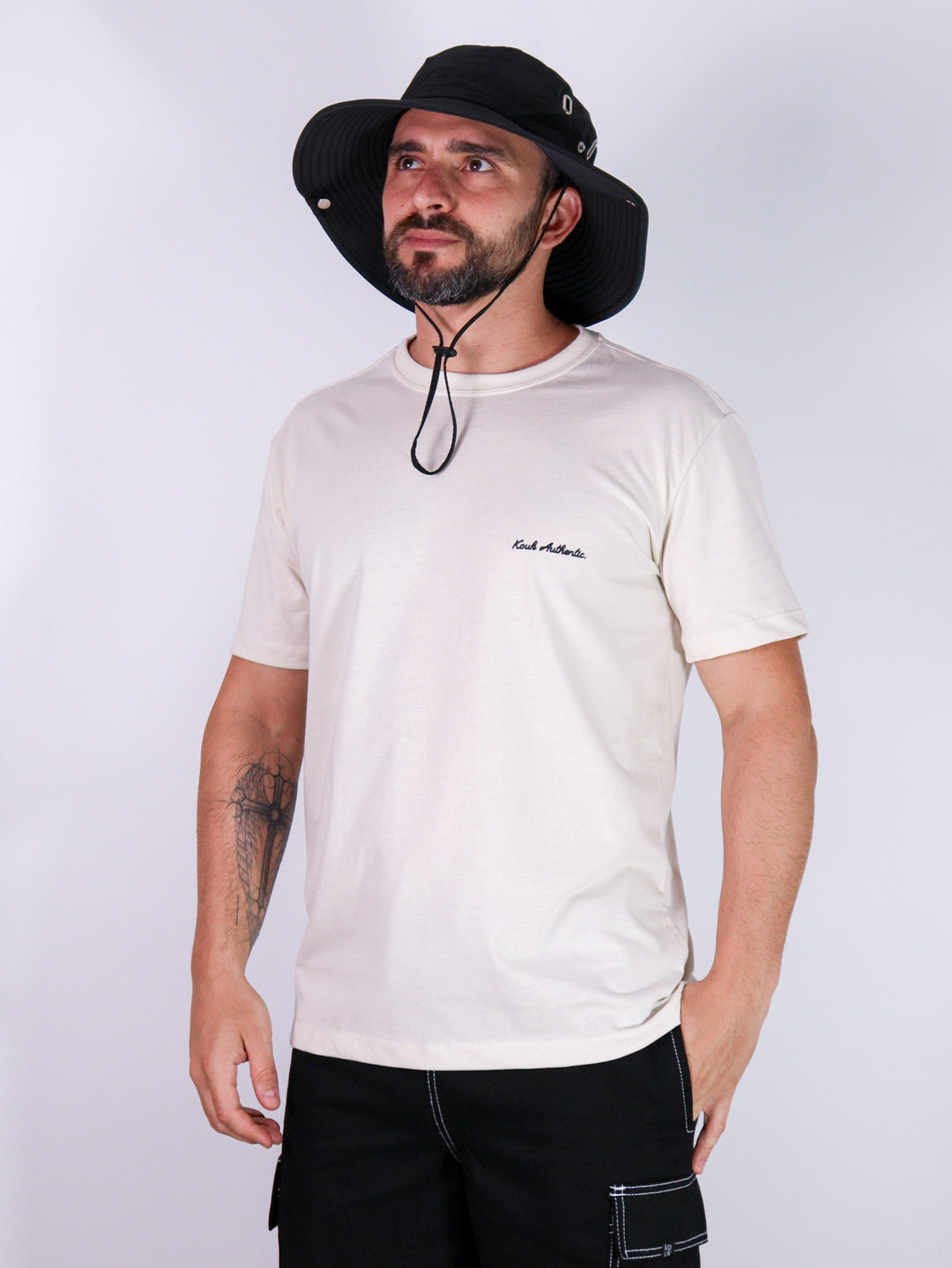 Modelo com camiseta branca da marca Kouk Authentic, logo verde na lateral esquerda, manga média curta. Produto a pronta entrega com desconto no frete para todos Brasil