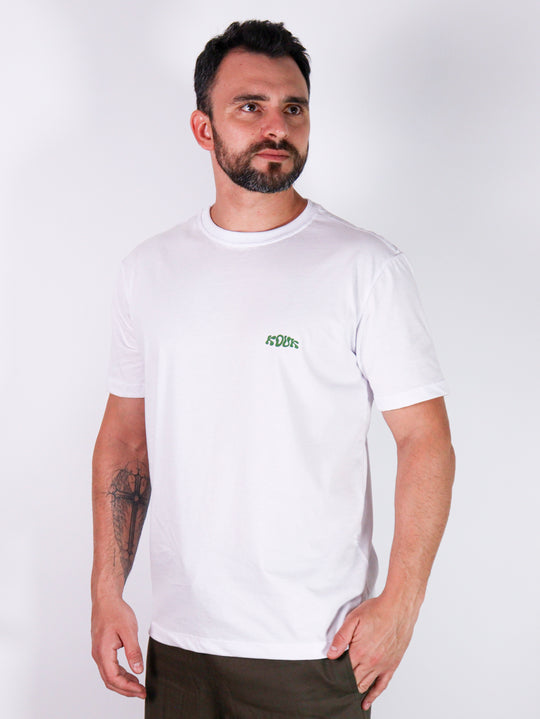 Modelo com camiseta branca da marca Kouk Authentic, logo verde na lateral esquerda, manga média curta. Produto a pronta entrega com desconto no frete para todos Brasil